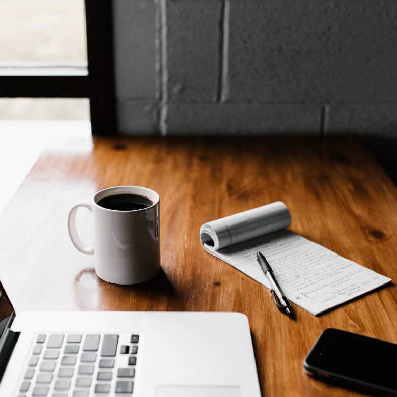 A MacBook Pro, a coffee, and a notepad & pen